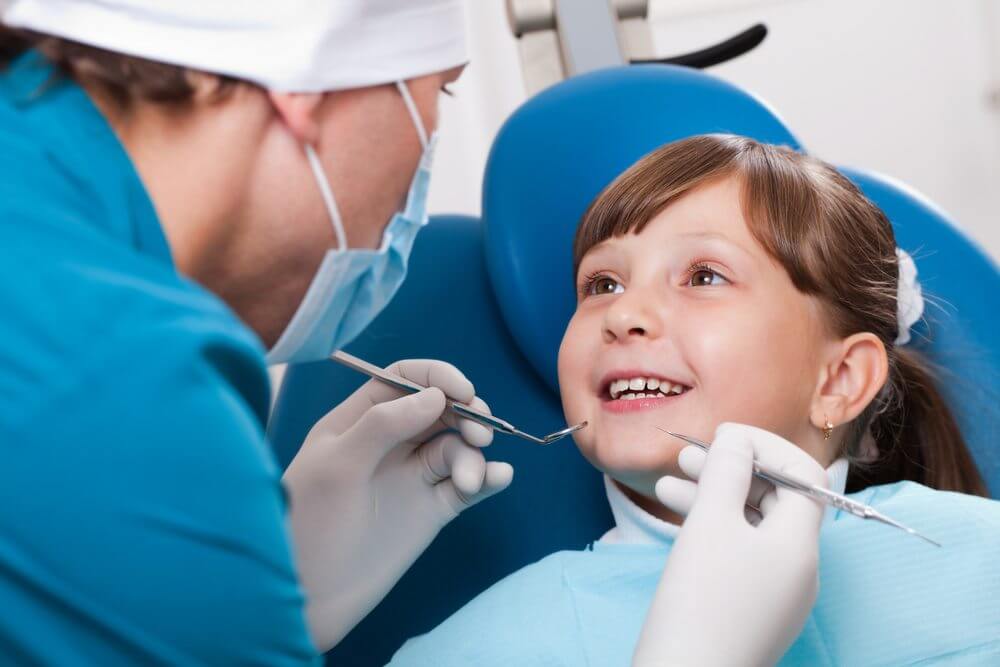 A dentist asking the young child to open her mouth so they can clean their teeth
